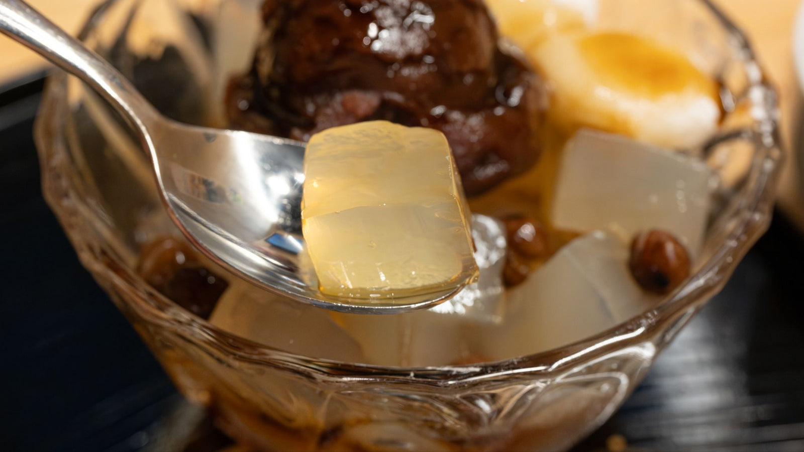 A close-up of a spoon scooping a piece of wobbly kanten from a bowl of anmitsu