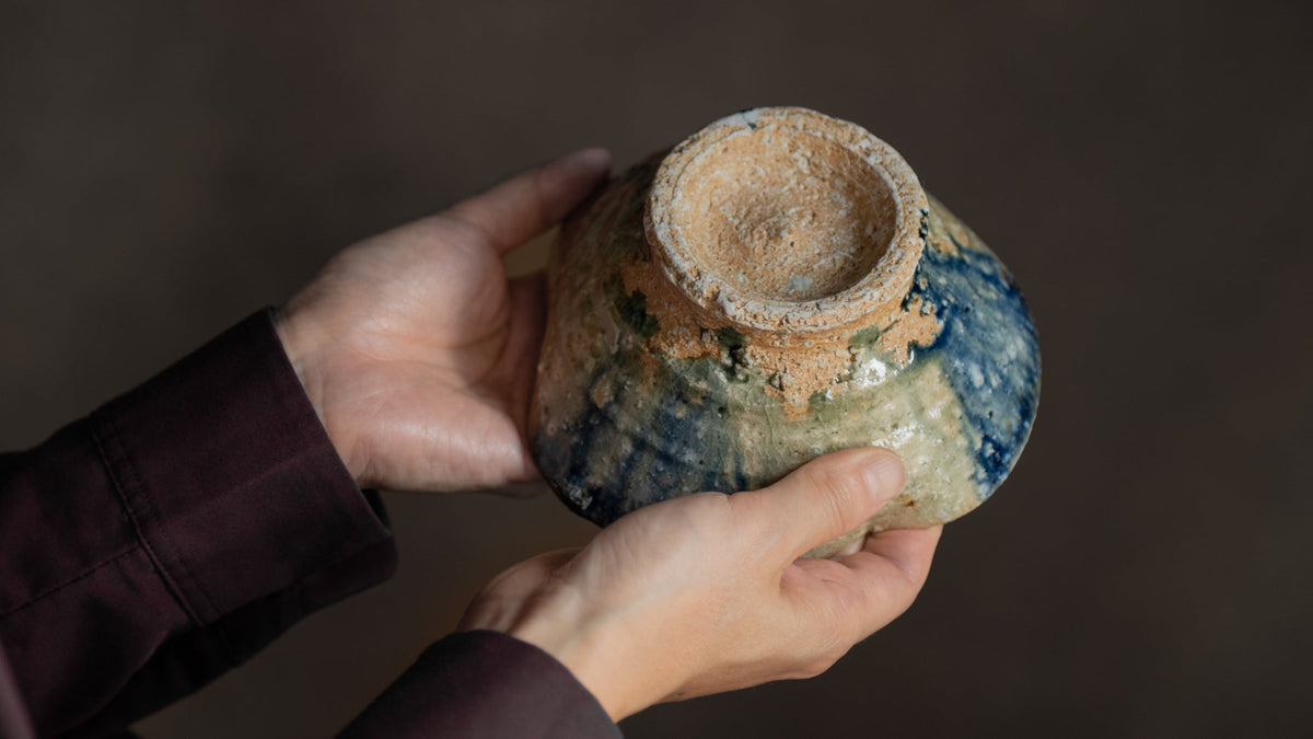 Hands turning a ceramic vessel upside down to examine the underside