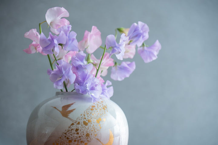 Pink and purple sweet peas arranged in a porcelain vase with gold crane design