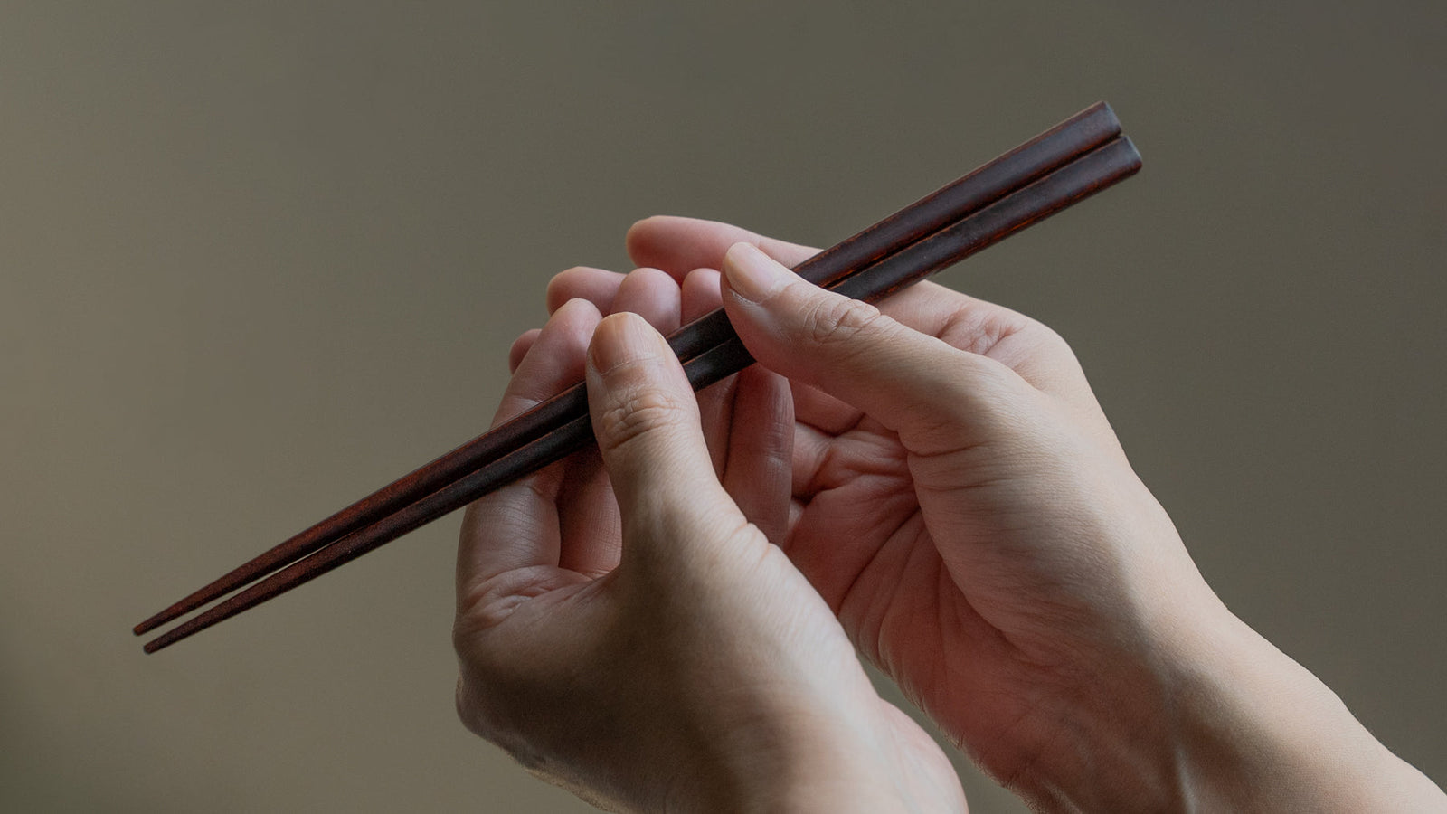 Hands gently holding a pair of lacquered chopsticks