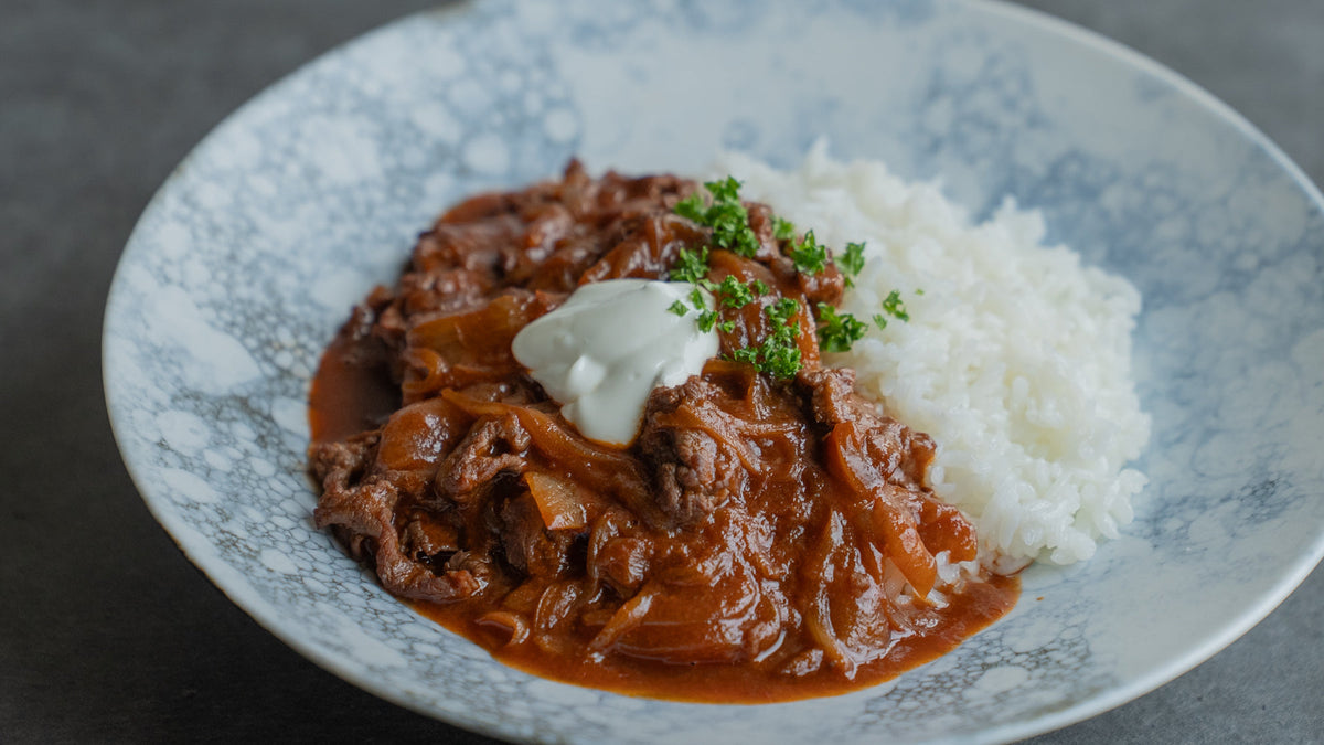 A bowl of hayashi rice with a rich, dark glossy sauce served over white rice, finished with a spoonful of yogurt